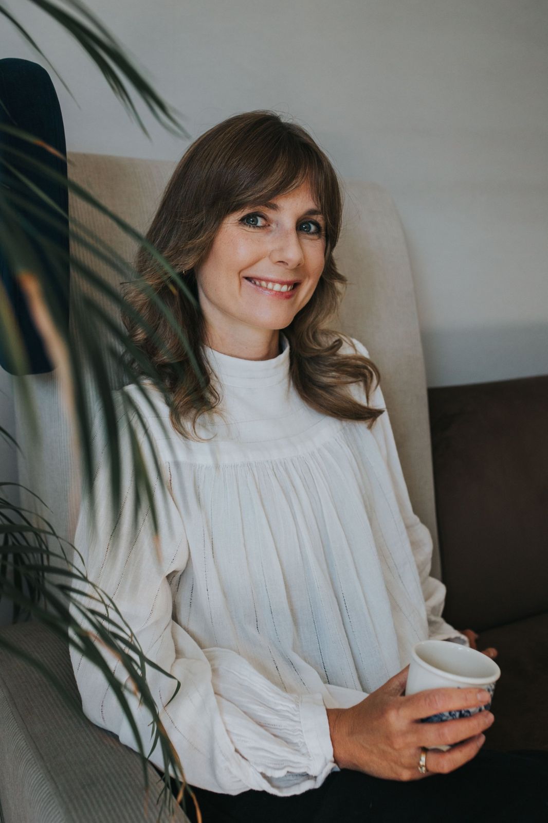 Uśmiechnięta Hanna Wojtaszek-Mikulska na kanapie, z filiżanką